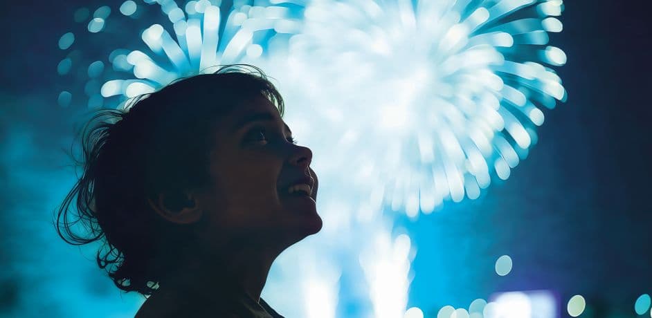 Ein Kind blickt in den Nachthimmel. Im Hintergrund ist ein Feuerwerk zu sehen. 